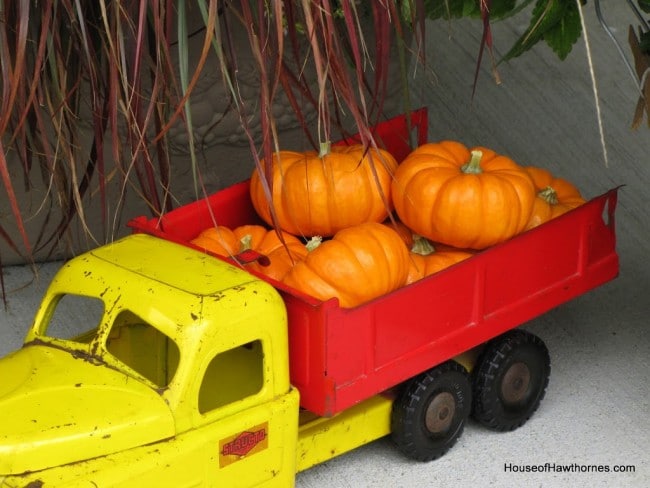 Fun fall front porch decor using traditional cornstalks, Indian corn, gourds and mums along with the unexpected - a vintage toy truck loaded with pumpkins.