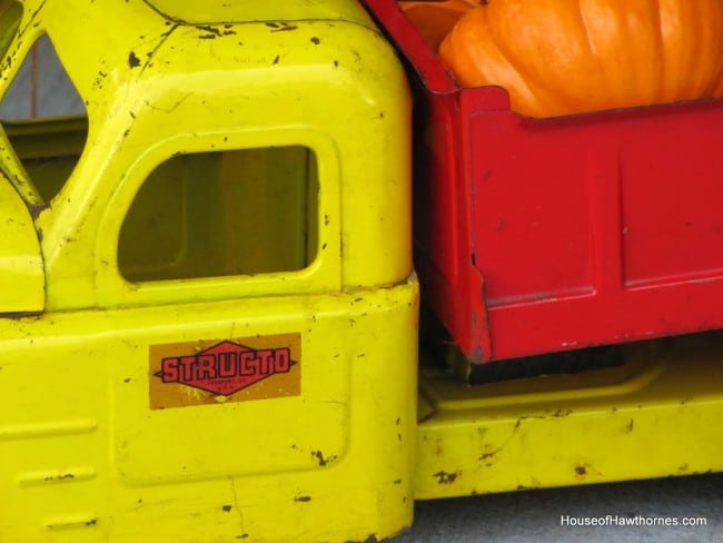 Fun fall front porch decor using traditional cornstalks, Indian corn, gourds and mums along with the unexpected - a vintage toy truck loaded with pumpkins.