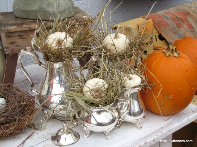 Silver plated tea sets with pumpkins and hay in them.