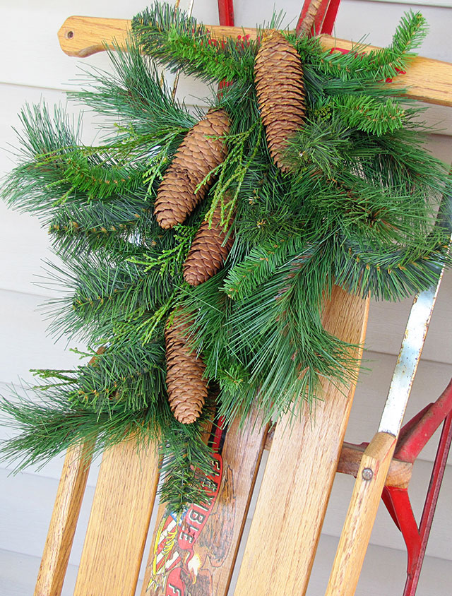 Greenery hung on a Radio Flyer sled used as Christmas decorations on the porch.