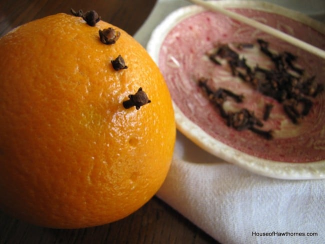Using a skewer to poke holes in an orange in order to put cloves in it.