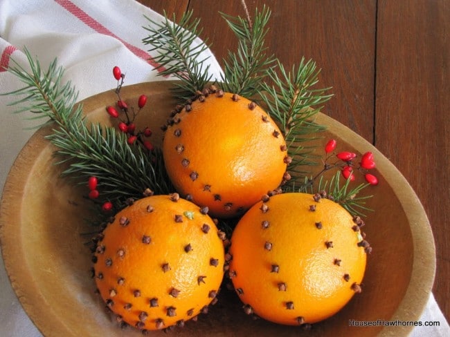 Wooden bowl of three oranges made into orange clove pomander balls.