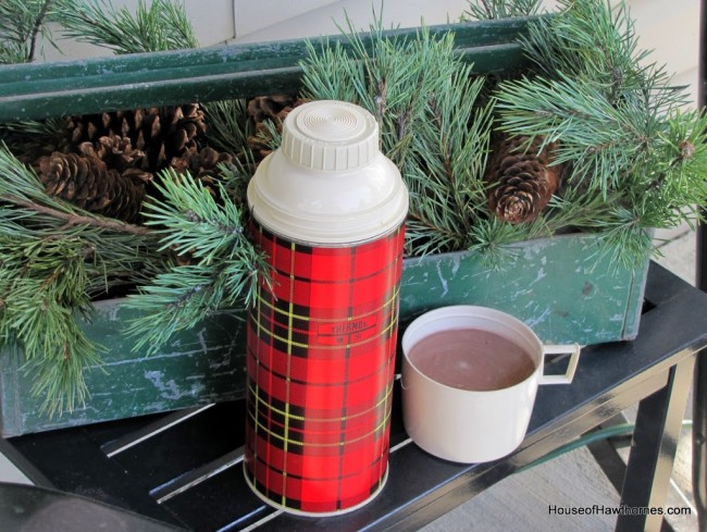 Red plaid thermos and a green tool caddy used as Christmas decor on the porch.