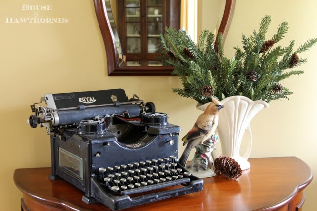 Vintage Royal typewriter, vase of pine greenery and a china bird figurine.