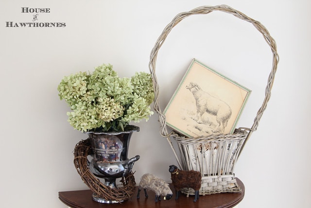 Vignette with silver wine bucket, hydrangeas, lambs and a vintage funeral basket. 
