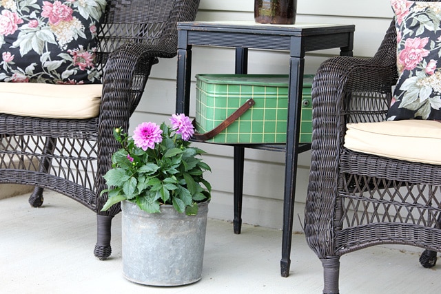 Vintage sap bucket setting on the porch with a dahlia flower planted in it. 