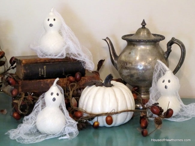Ghosts made from gourds setting on a blue cabinet with Halloween decor.