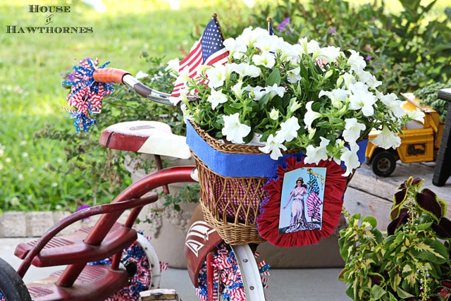 A vintage little red Tricycle decorated for the 4th of July with patriotic crepe papers, flags and flowers. A cute DIY project for patriotic porch decor. 