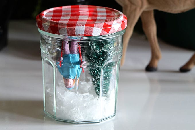 Upside down jelly jar with a red gingham lid -  being used to make a snow globe for the holidays. 