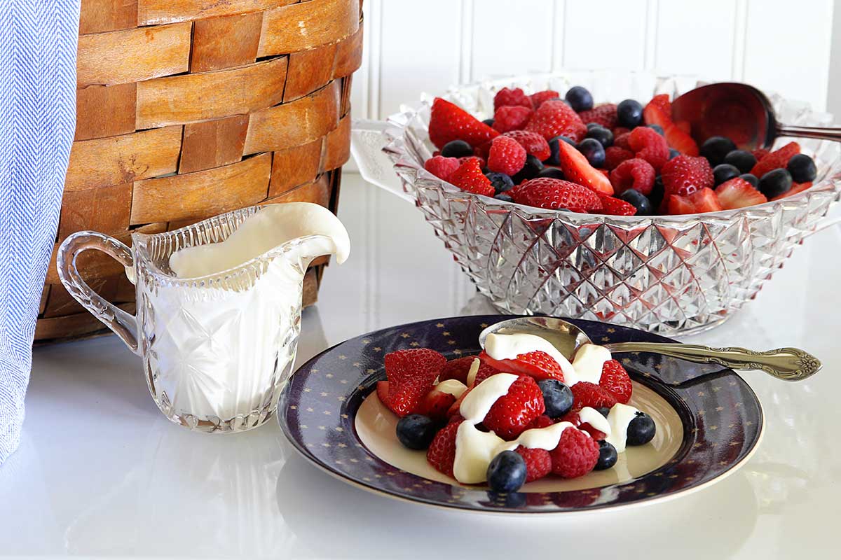 Bowl of mixed berries sitting next to pitcher of honey citrus dressing. 