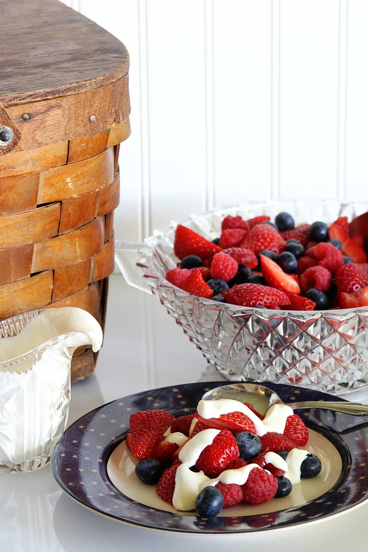 A summer fruit salad on a patriotic plate next to a wooden picnic basket.