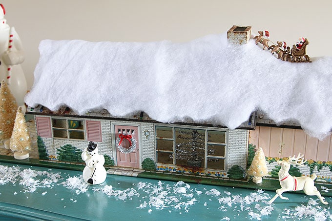 A mid-century modern Christmas dollhouse complete with a tiny little tinsel Christmas tree and Santa on the rooftop.