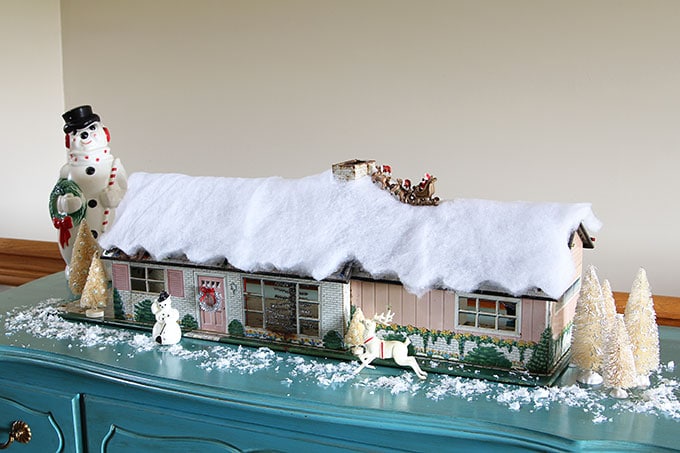 A mid-century modern Christmas dollhouse complete with a tiny little tinsel Christmas tree and Santa on the rooftop.
