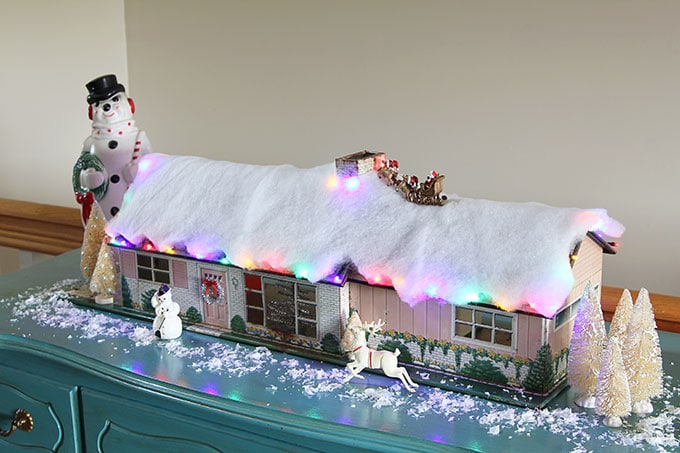 A mid-century modern Christmas dollhouse complete with a tiny little tinsel Christmas tree and Santa on the rooftop.