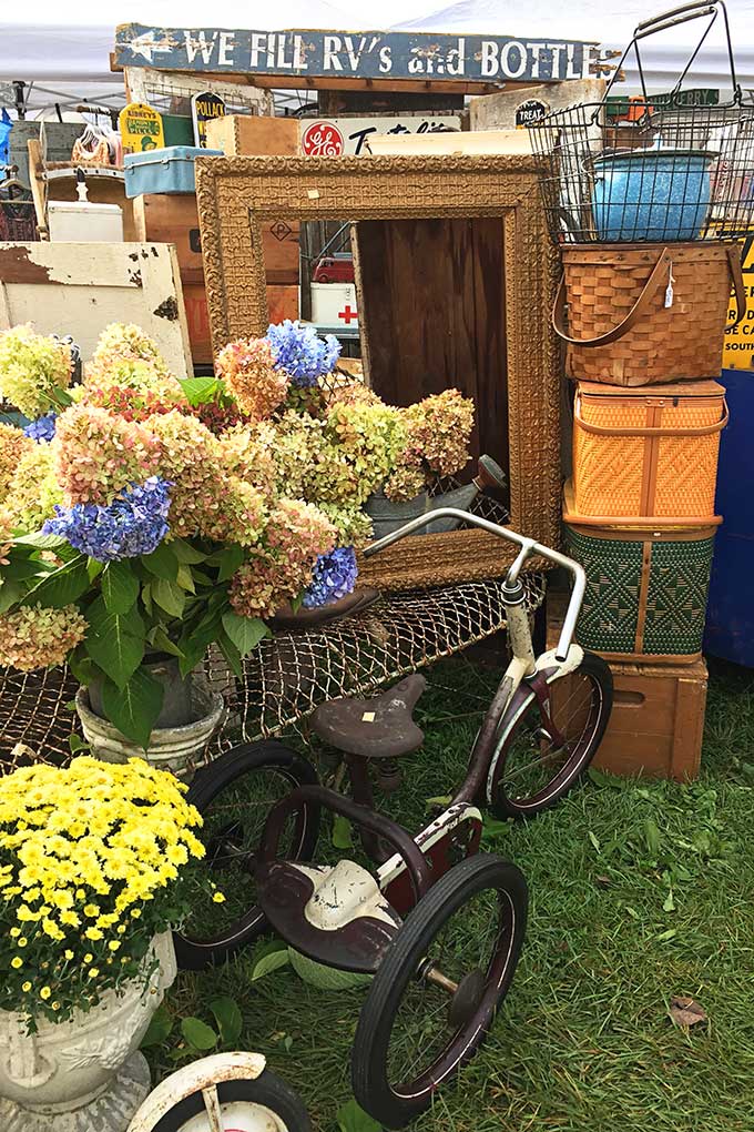 Farmhouse decor at the Country Living Fair including a tricycle, vintage picnic baskets and hydrangea.