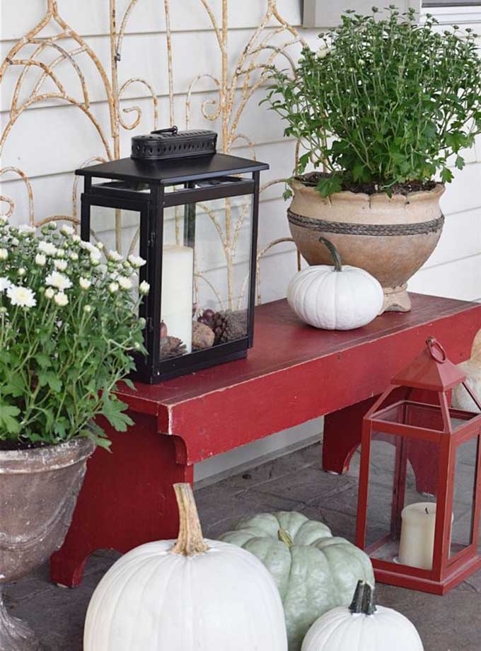 Red bench mixed with heirloom pumpkins and lanterns for outdoor fall decor from Timeless Creations.