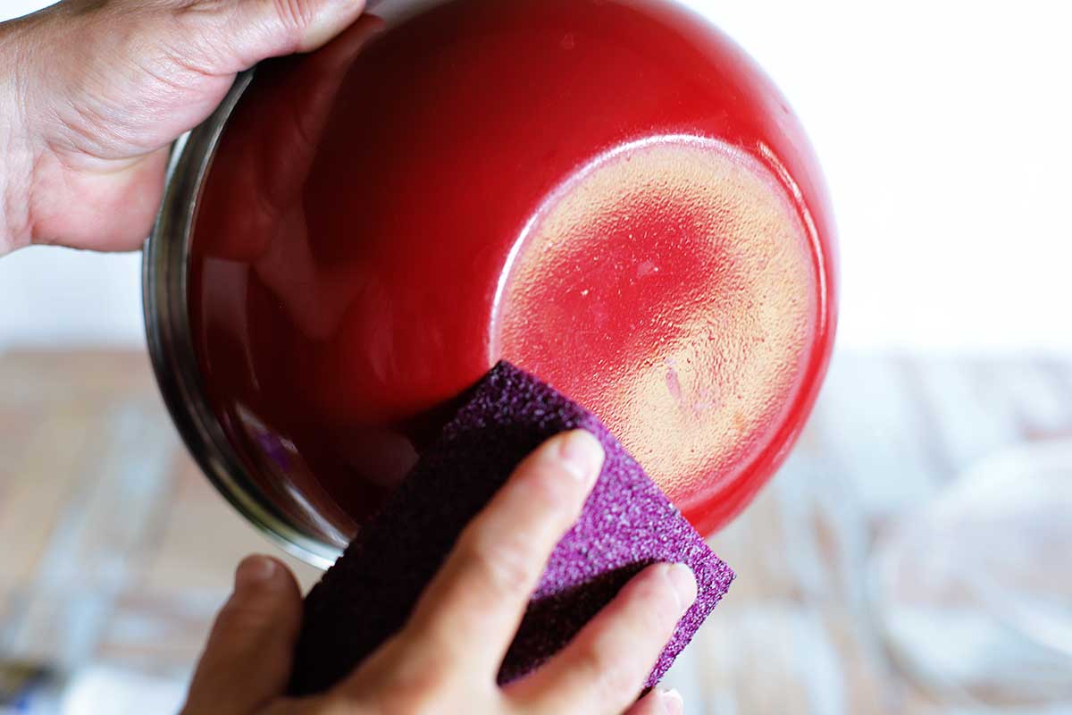 Sanding the bottom of a red bowl to be used to make an upcycled bird bath from thrift store glassware.