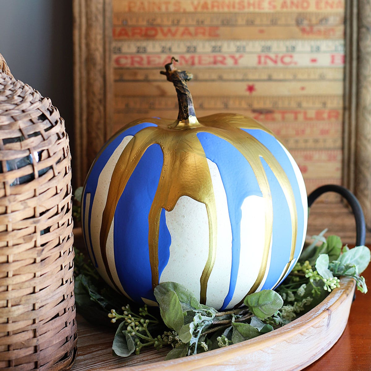 Pumpkin decorated by the paint pouring technique setting on a tray surrounded by rustic farmhouse decor.