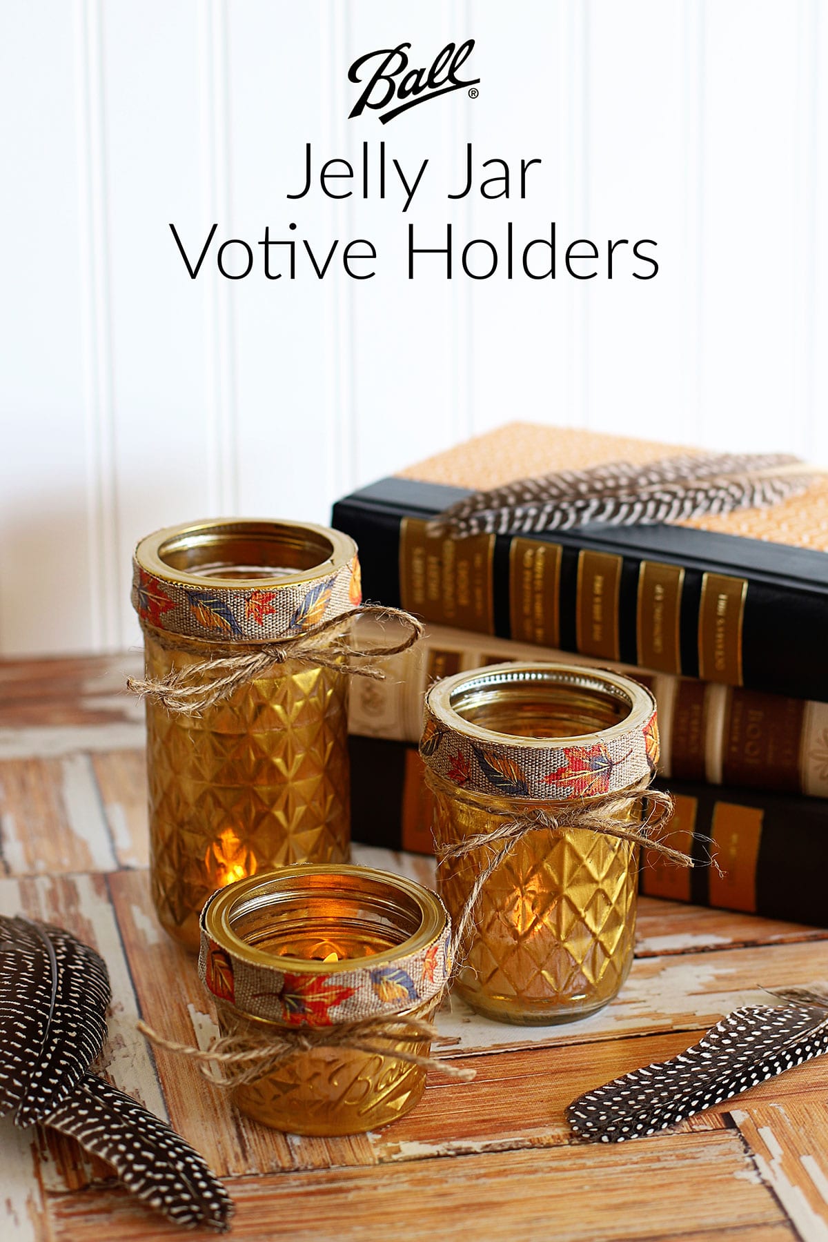 Gold votive holders made from mason jars are setting on a wooden background with feathers and books.