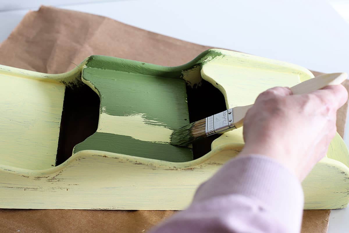 Green paint being applied to a wooden mail holder.