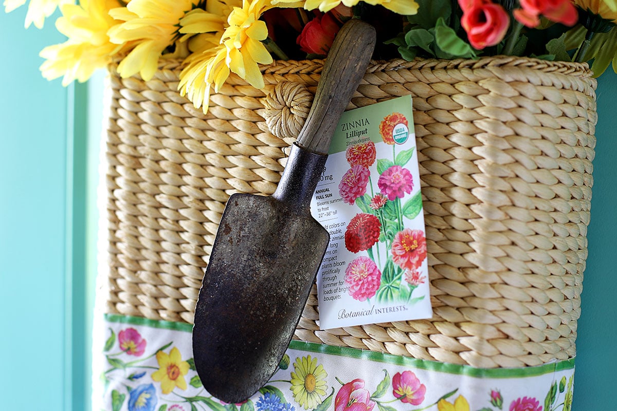 Close up of a garden trowel and packet of zinnia seeds as part of a summer door wreath.