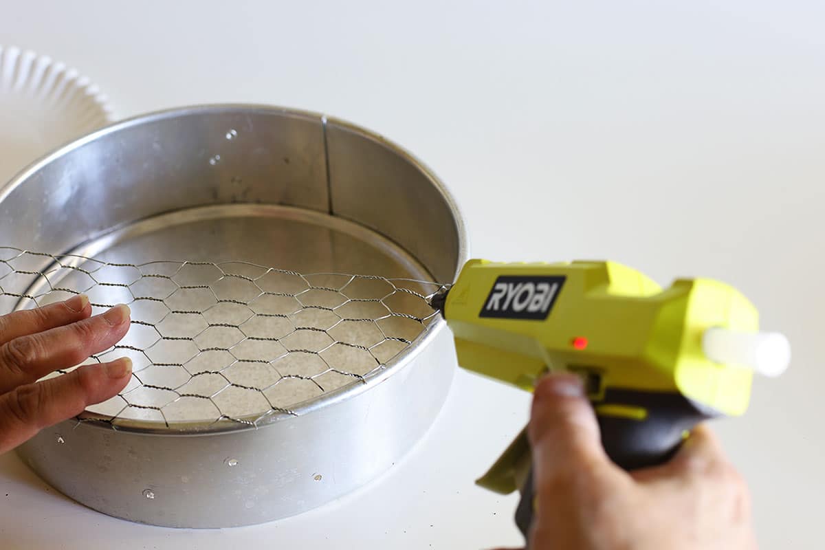 Gluing the chciken wire to the edge of the cake pan.