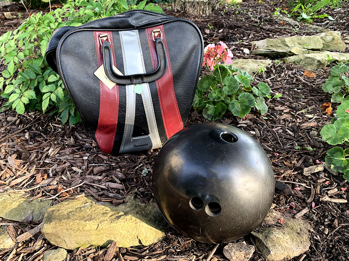 Black bowling ball and bowling ball bag being used to create mosaic garden art.