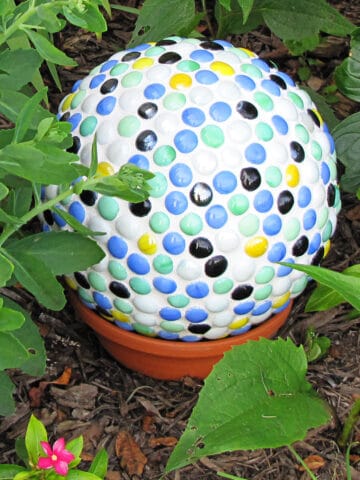 Bowling ball yard art made from covering a bowling ball with mosaic gems and displaying in the garden.