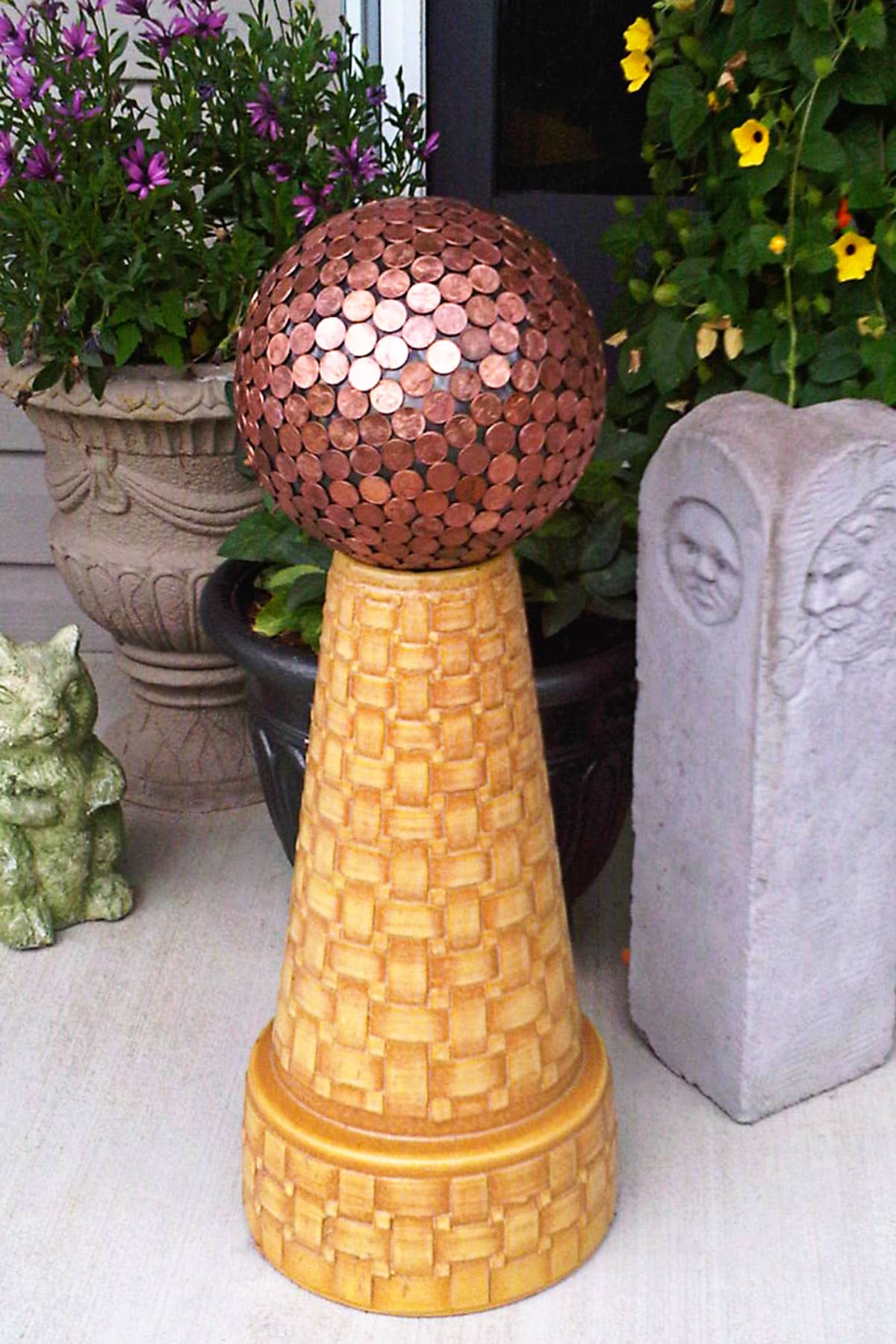 Bowling ball covered in pennies and used as garden art.