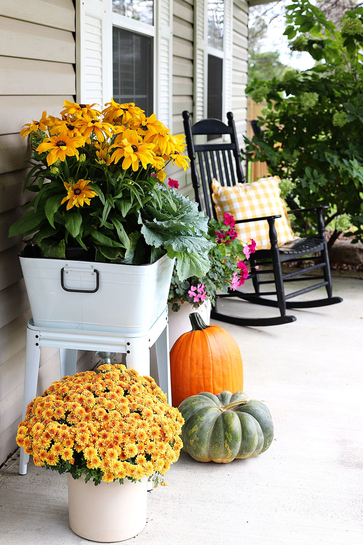 Side view of Back-eyed Susan, ornamental cabbage and crotons in an enamelware wash tub for fall porch decor. A black rocker with yellow buffalo check pillow in the background.
