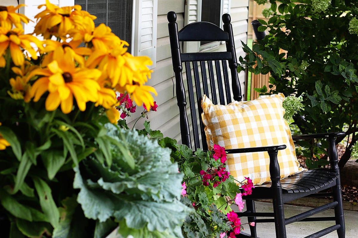 Bright and cheerful fall flowers and a black rocker with a yellow buffalo check pillow.