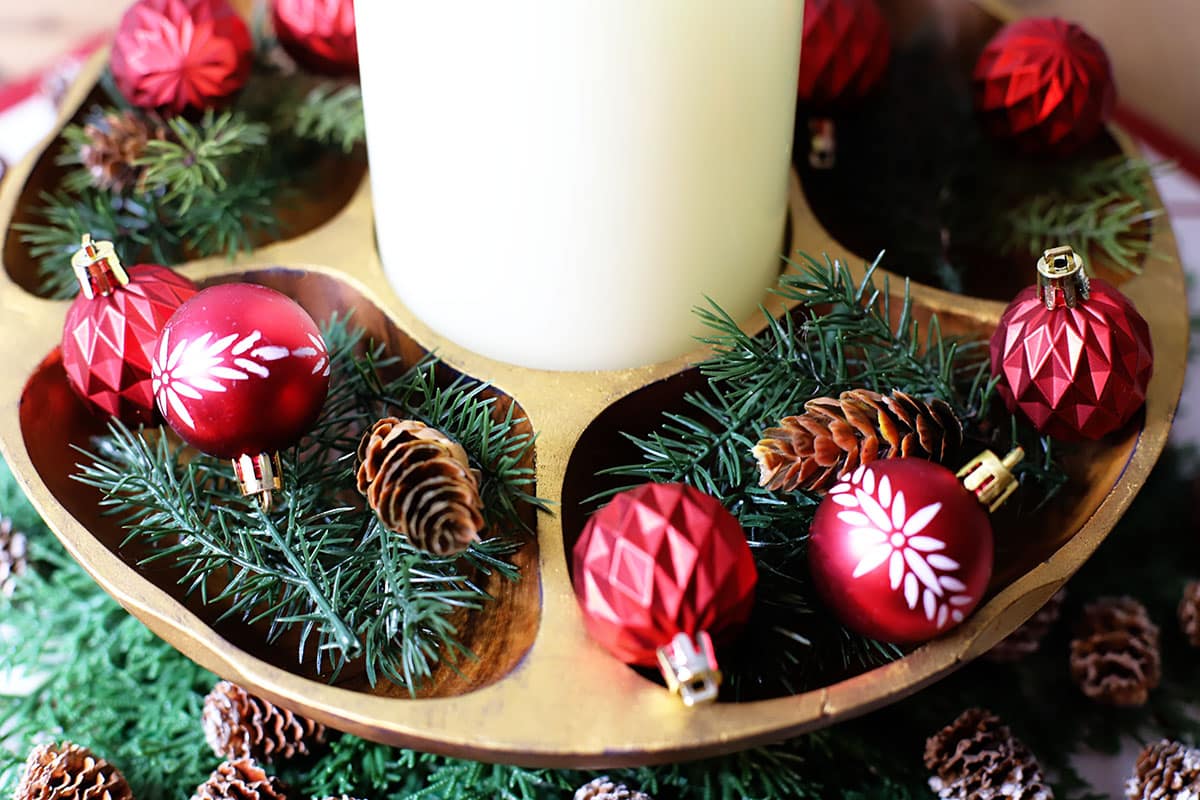A painted vintage wooden bowl filled with a candle, winter greenery and red Christmas ornaments.