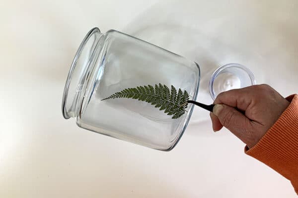 Applying fern leaves to a glass jar.