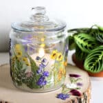 Glass jar decoupaged with dried pressed flowers setting on a wooden tree slab.