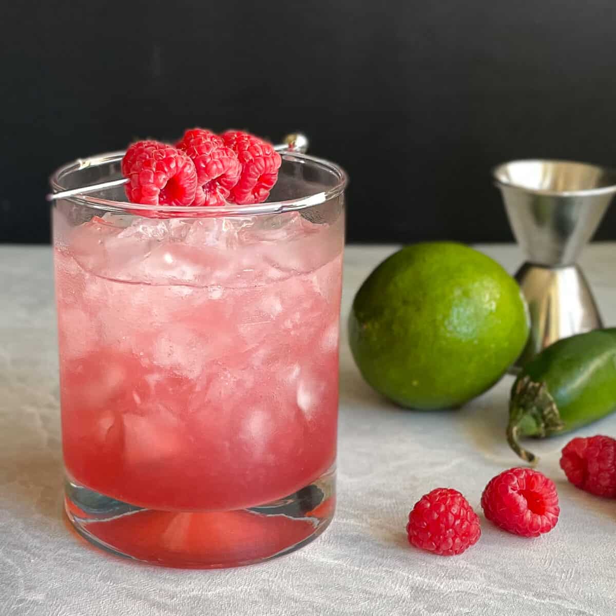 A raspberry bramble cocktail in a glass with raspberries garnishing the top of the glass.
