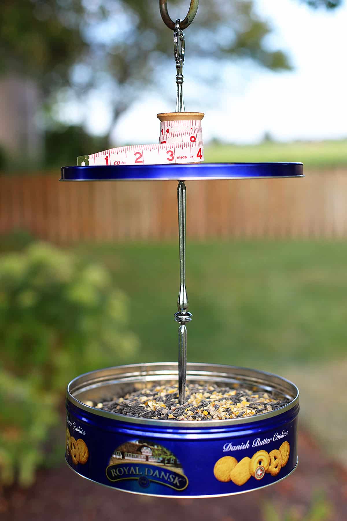 DIY bird feeder made from a Danish butter cookies tin. The top of the bird feeder has a spool and measuring tape on it. 