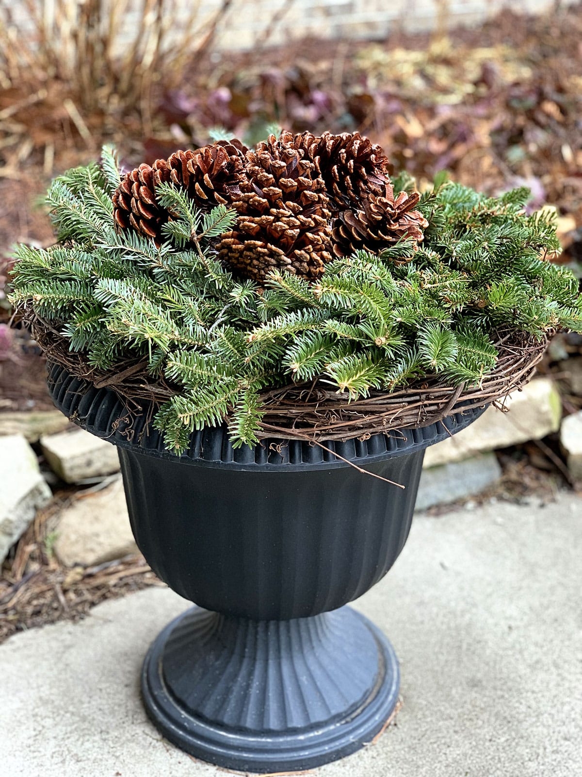 Winter porch pot for the holidays using pine cones, grapevine wreath and an inexpensive fresh greenery christmas wreath.