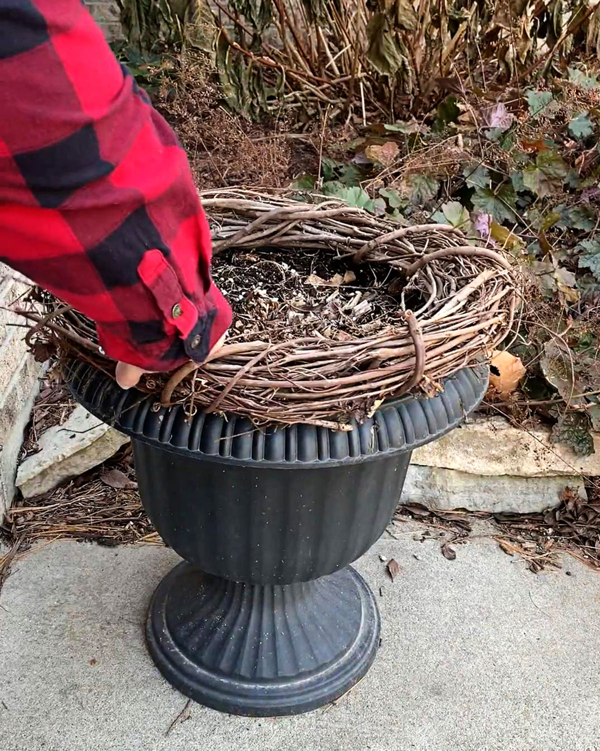 Placing a plain grapevine wreath on an urn for winter porch decor.