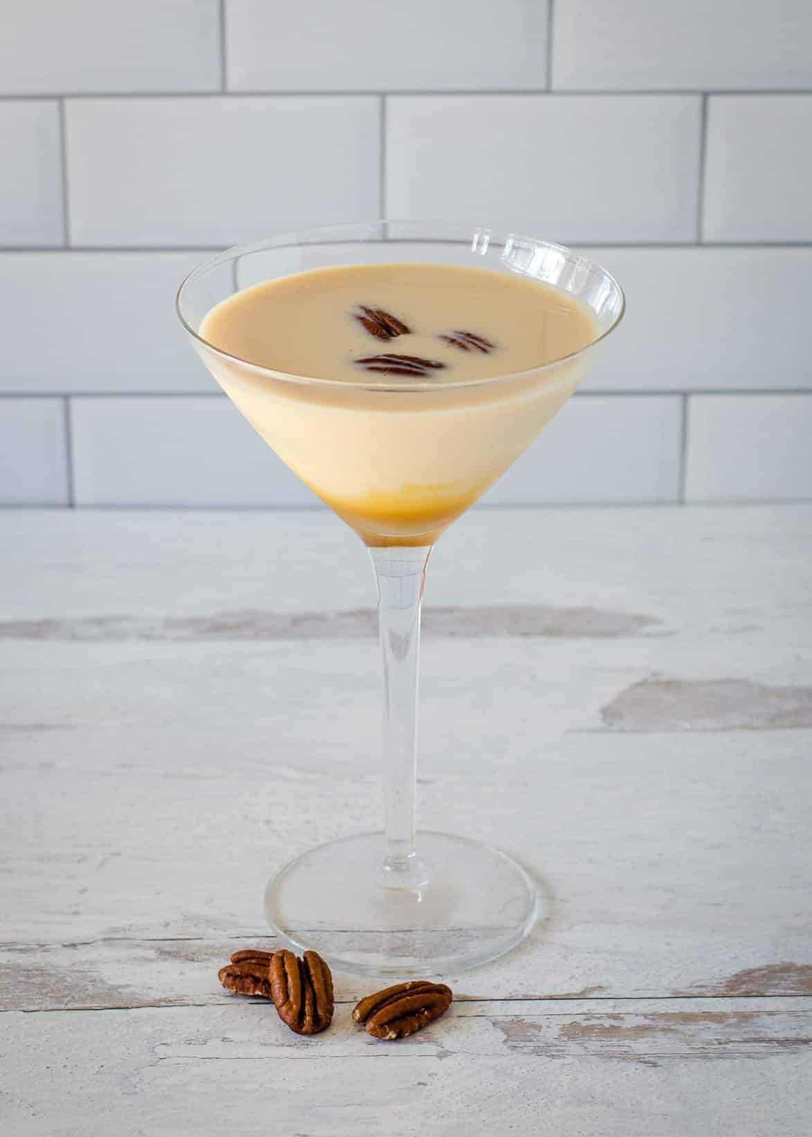 A pecan pie martini in a traditional martini glass with pecan pieces.