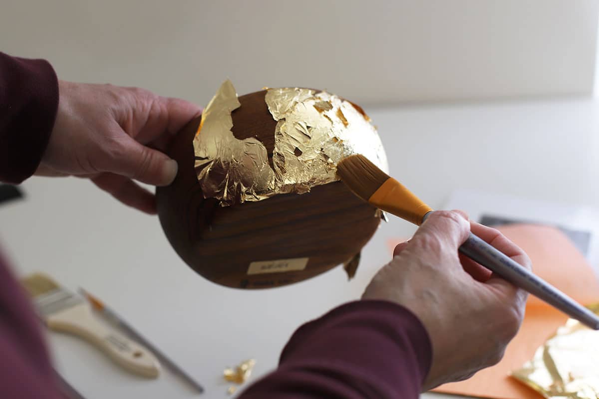 Using a paint brush to brush off excess gold leaf.