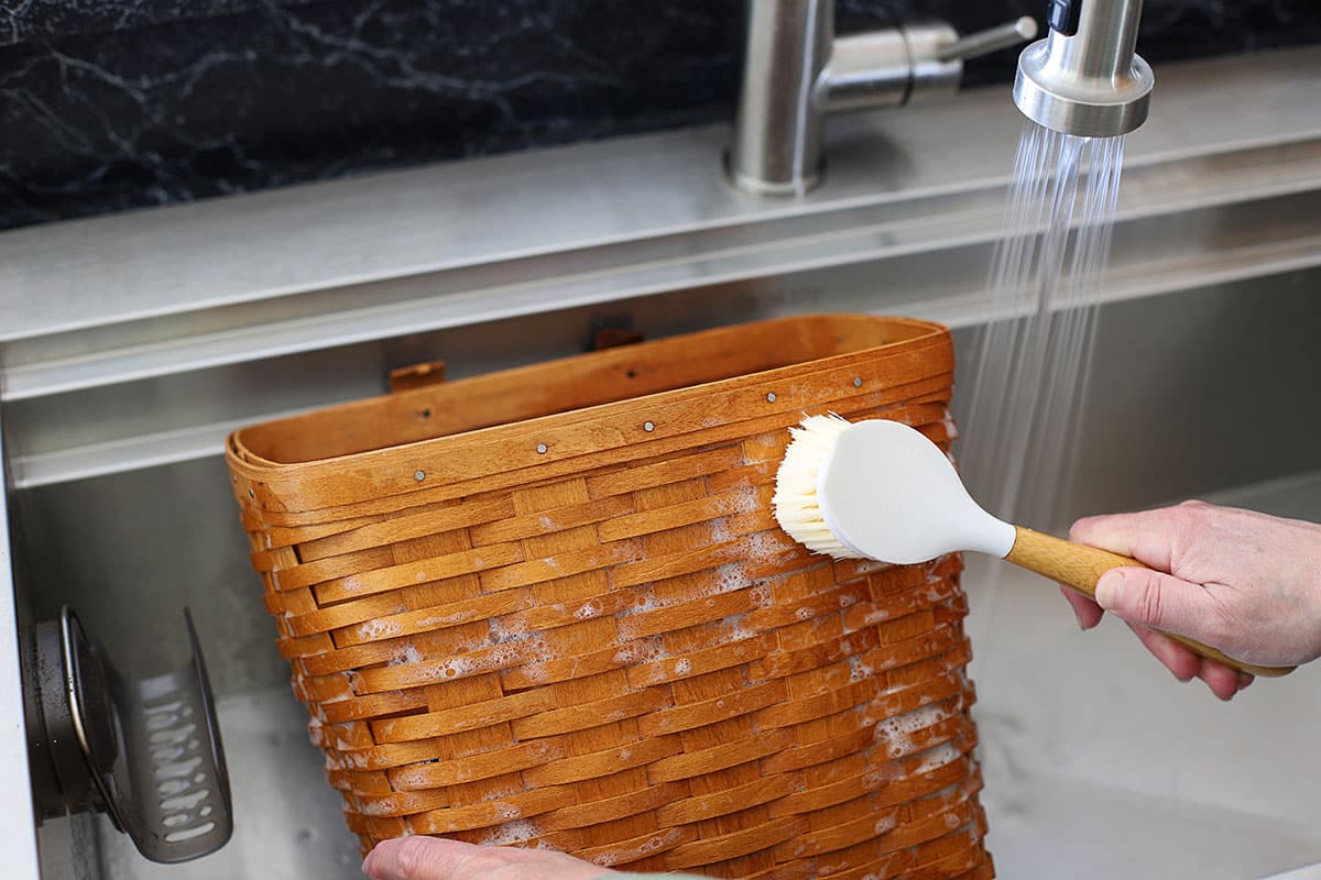 Washing a Longaberger basket in the sink with soap and water to remove stains.