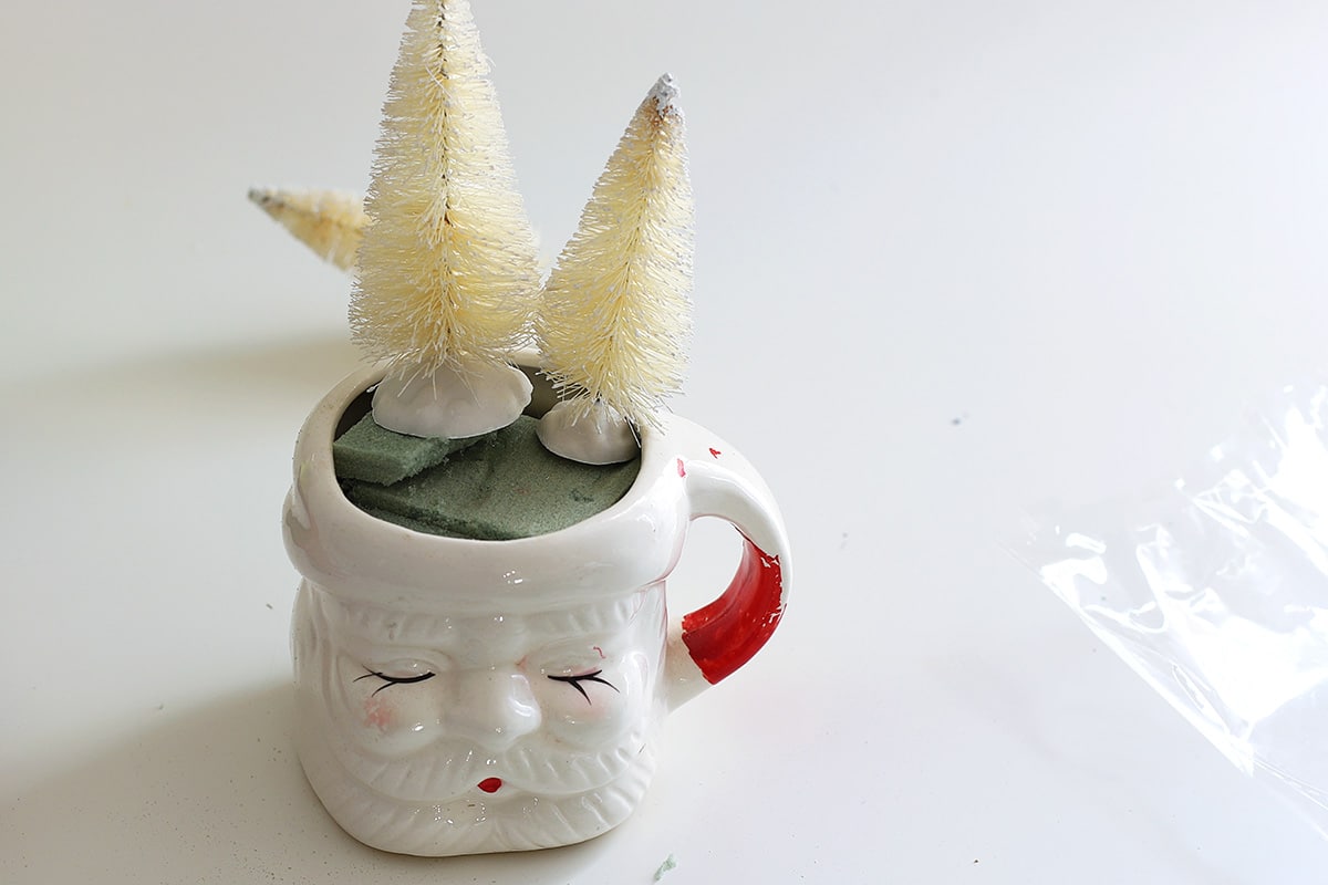 Two white bottle brush trees in a vintage Santa mug. 