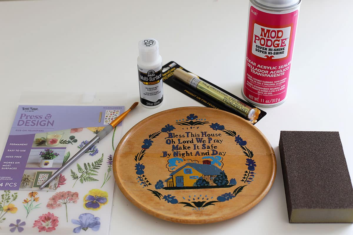 Supplies for upcycling a kitschy wooden kitchen plaque from the 1960s. Includes paint, acrylic sealer and rub-on transfers.
